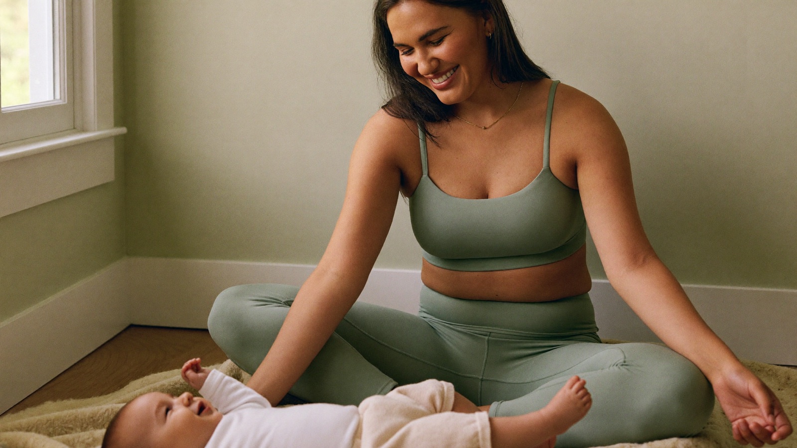 A smiling mum sitting with her baby during a gentle home session
